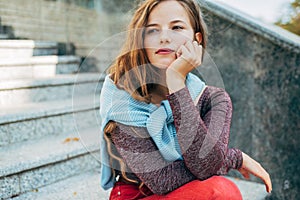 Candid portrait of a pensive female takes a rest outside on the street. Thoughtful young student woman sitting next to the college