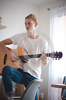 Candid portrait of a young artist in the living room. The singer holds his guitar and strums a song. Home quarantine. Fulfilling