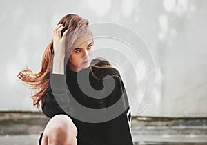 Candid portrait of young beautiful long hair girl fashion model hipster in black hoodie on wall background