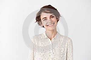 Candid portrait of young beautiful woman smiling happy at camera, looking friendly, standing on white background