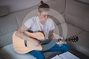 Candid portrait of a young singer playing an acoustic guitar and singing in a hymn book in a lighted, grey-toned living room. A