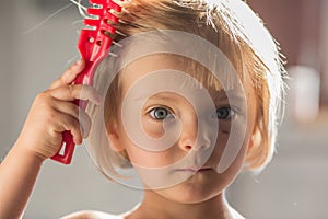 Candid serious thinking or sad young baby caucasian blonde girl with small scratch comb with hair brush at home