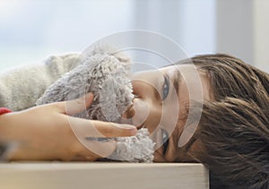 Candid shot adorable kid lying on table looking at camera with smiling face, Child boy relaxing at home playing with soft toy,