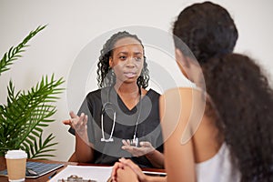 Candid shot of Black female doctor explaining to patient during GP consultation