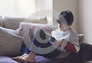 Candid shot cute little boy watching cartoons on tablet, Portrait of School kid sitting on sofa with serious face playing games on