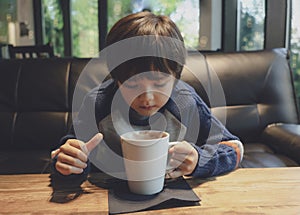 Candid shot kid drinking hot chocolate in the cafe with warm tone, Healthy child boy blowing hot drink at coffee shop in winter