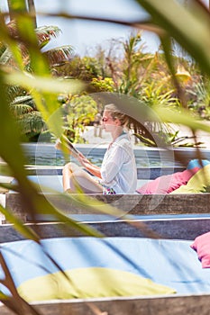 Candid shot of lady reading book and relaxing in lush tropical garden.