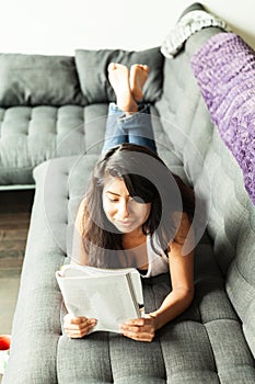 Candid Spanish woman smiling and reading a magazine. Home on a sofa