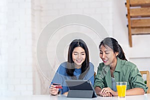 Candid of young attractive asian two girls sitting at home holding discount credit card in hand paying for shopping online at