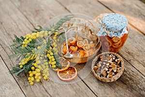 Candied orange spiral peel with sugar syrup in a glass jar and plate near the saucer with walnuts, mimosa and bread