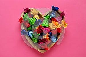 Candies in colorful wrappers on pink background, top view