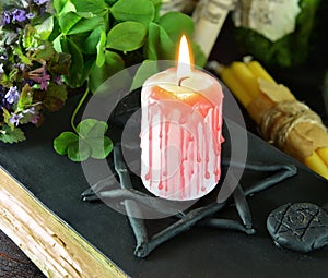 Candle on black magic book with clover