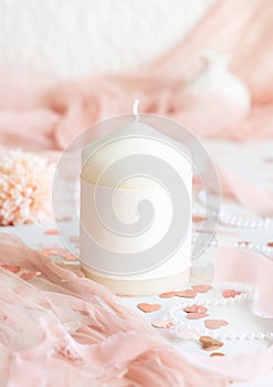 Candle with blank label near pink decorations, hearts and tulle on white table close up, mockup
