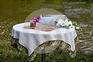 Candle and a bouquet of flowers are on the table against the riv