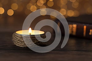 Candle burning with bright flame and closed holy bible book on wooden table with bokeh background