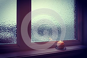 Candle burning near a frosted window in twilight