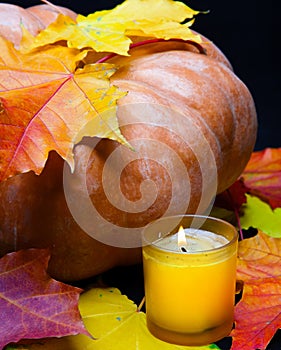 Candle burns and pumpkin with red maple leaf