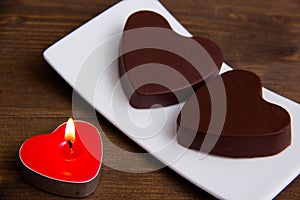 Candle and chocolates in a heart shape on wood close