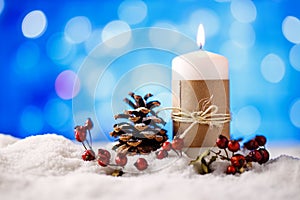 Candle and christmas decoration in snow with blue light background.