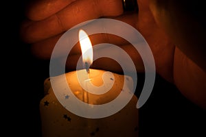 Candle on a dark background. A hand protects the flame