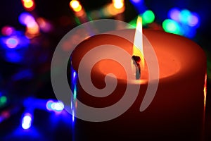 A candle with flame with lights in the background.