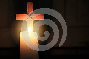 The candle glows in front of the cross. Christmas, Easter and religious background with copy space