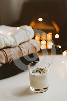 Candle, knitted sweaters, christmas decorations against bokeh lights background. Christmas hygge cozy mood still life