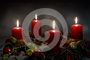Candle light in the night, part of an Advent wreath with four red candles and Christmas decoration against a dark background, copy