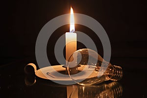 Candle and a lightbulb on a black background. A concept of electricity crisis in South Africa.