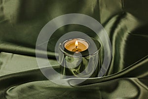 A candle in a metal holder on a dark olive green silk tablecloth. Stylish decor.