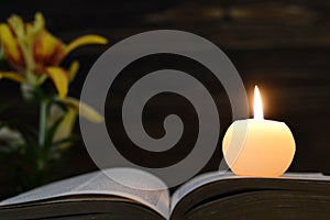 Candle, opened book and flowers on dark background