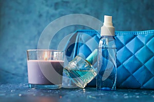 Candle perfume and cosmetic bag with water drops in shallow depth of field on blue background