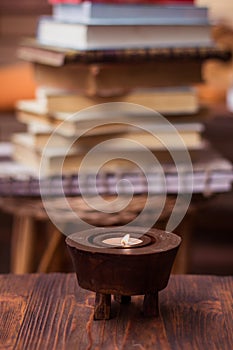 Candle on wooden table with books in background