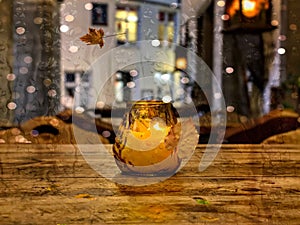 candle on wooden table in city street raing drops on window  falling yellow Autumn leaves in Tallinn old town  seasdon