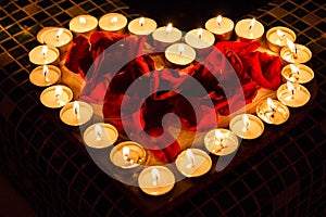 Candlelights shine in form of the heart with red roses petals