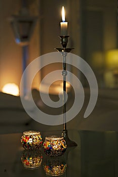 Candles burning on the table in the dark. Candlestick and candleholders at home in dim lighting. Cozy, relaxing and warm mood