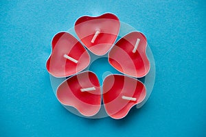 Candles in the form of red hearts on a blue background are laid out in the shape of a flower.