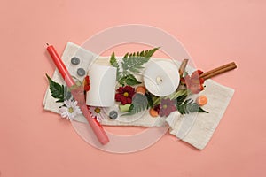 Candles, fresh flowers, cinnamon and green leaves are artistically decorated on a pink background with white fabric. Get creative