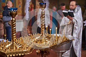 Candles in a golden chandelier in the Orthodox Church, close-up, priest with parishioners in the background out of focus