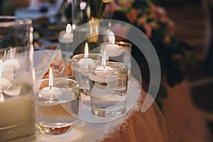 Candles with lights in glasses with water, stylish wedding decor for evening ceremony or at reception in restaurant. Spiritual