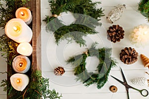 Candles and rustic christmas wreath with pine cones on white wooden table