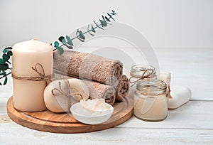 Candles, soap and a set of brown towels with a branch of eucalyptus on a white wooden background.