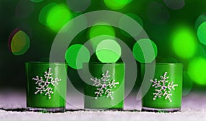 Candles standing in snow with defocussed fairy lights, green bokeh in the background, Festive Christmas background