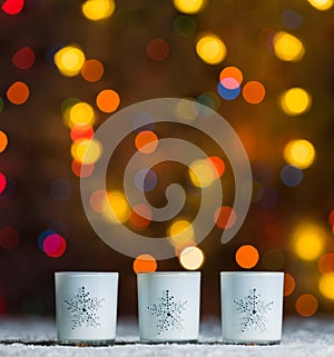 Candles standing in snow with defocussed fairy lights, orange or golden bokeh in the background