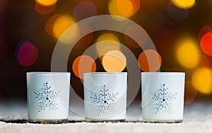 Candles standing in snow with defocussed fairy lights, orange or golden bokeh in the background