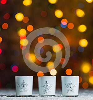 Candles standing in snow with defocussed fairy lights, orange or golden bokeh in the background photo