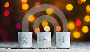 Candles standing in snow with defocussed fairy lights, orange or golden bokeh in the background