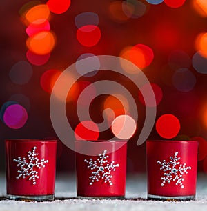 Candles standing in snow with defocussed fairy lights, red bokeh in the background, Festive Christmas background