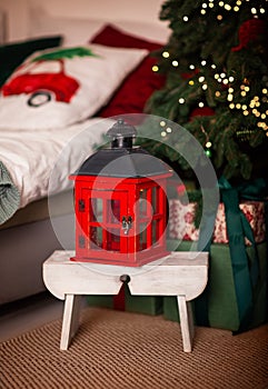 A candlestick in the form of a red retro lantern stands on a stool near the Christmas tree.