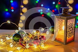 Candlestick with glowing candle, glowing lights and different colors balls are on the shiny table/background.